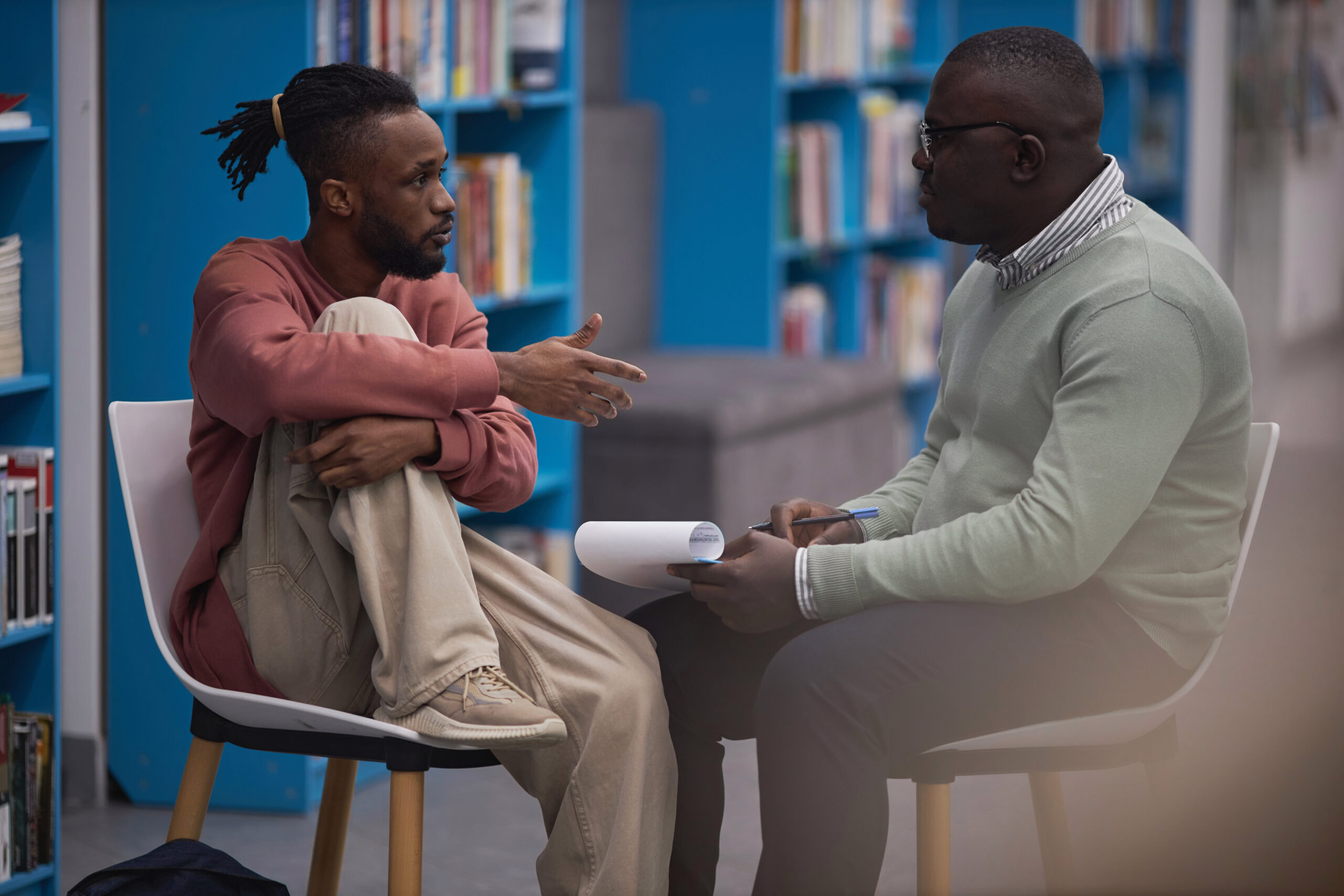 Side view portrait of black student talking to mental health therapist or guidance counselor in college library